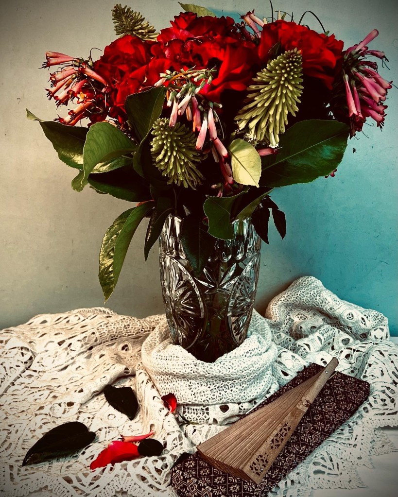 Still life featuring flowers in a vase and a wooden fan